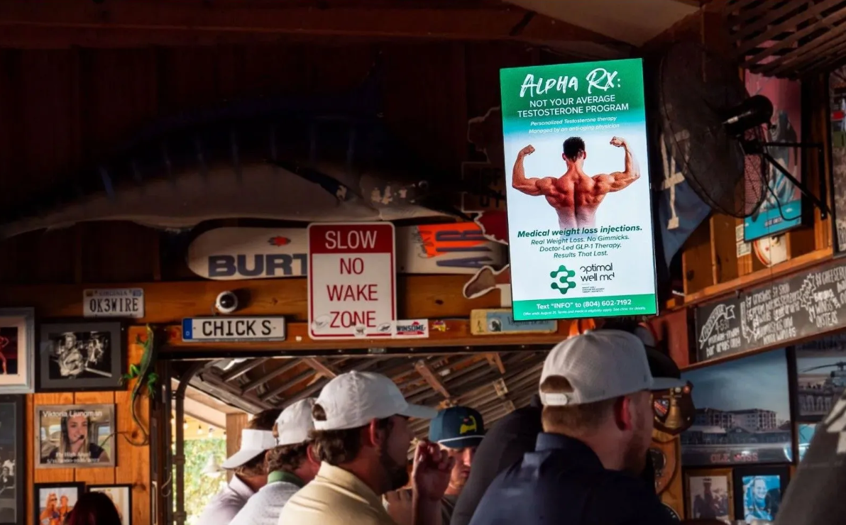 Digital advertising screen displaying a client ad inside a busy Virginia Beach restaurant